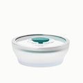 A 4-Cup Glass Round Shallow Dish with a clear, round lid featuring a teal silicone seal and pull tab—perfect for reheating leftovers or steaming green beans—is shown against a white background.