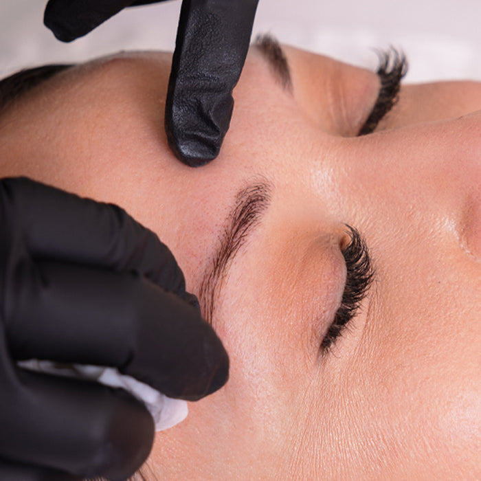 Person getting eyebrow tattoo with black gloves on a neutral background