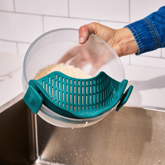 A hand holds a bowl with rice and a Clip-on Strainer attached, draining water into a sink like a compact colander, against a backdrop of white tiled wall.