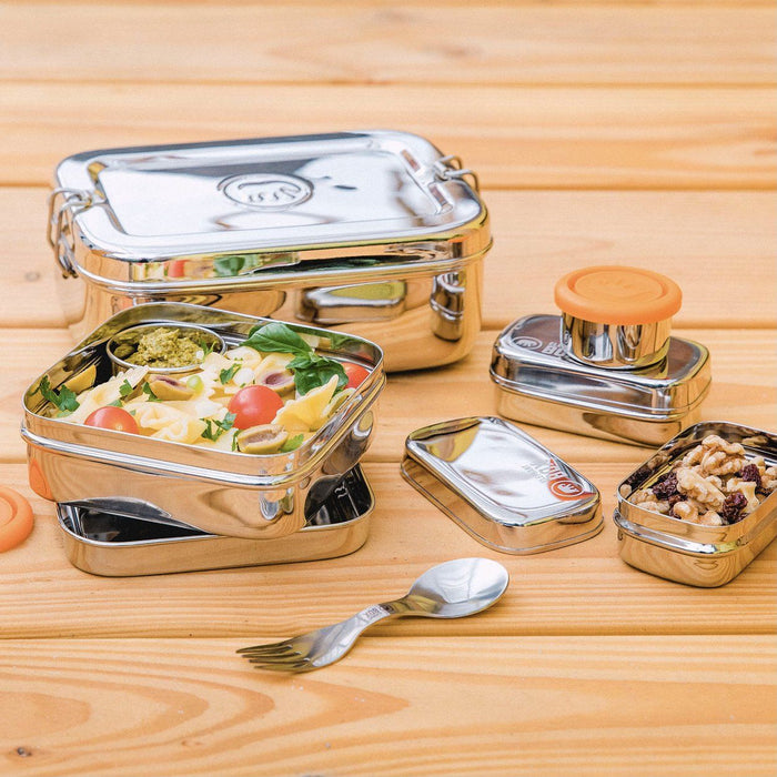 a set of stainless steel lunch boxes and snack containers from elephant box - including a square salad box with pasta salad, two dressing pots with lids and two snack boxes with mixed fruit.