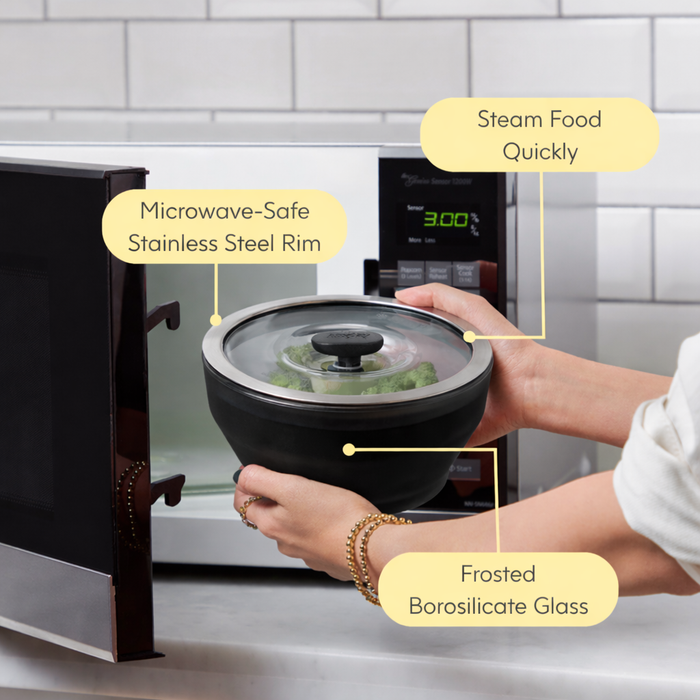 A person places an exclusive Onyx Collection frosted borosilicate glass bowl with a stainless steel rim into a microwave, highlighting its features—steam food quickly, microwave-safe stainless steel rim, and premium frosted borosilicate glass—making it perfect for effortless microwave meals.