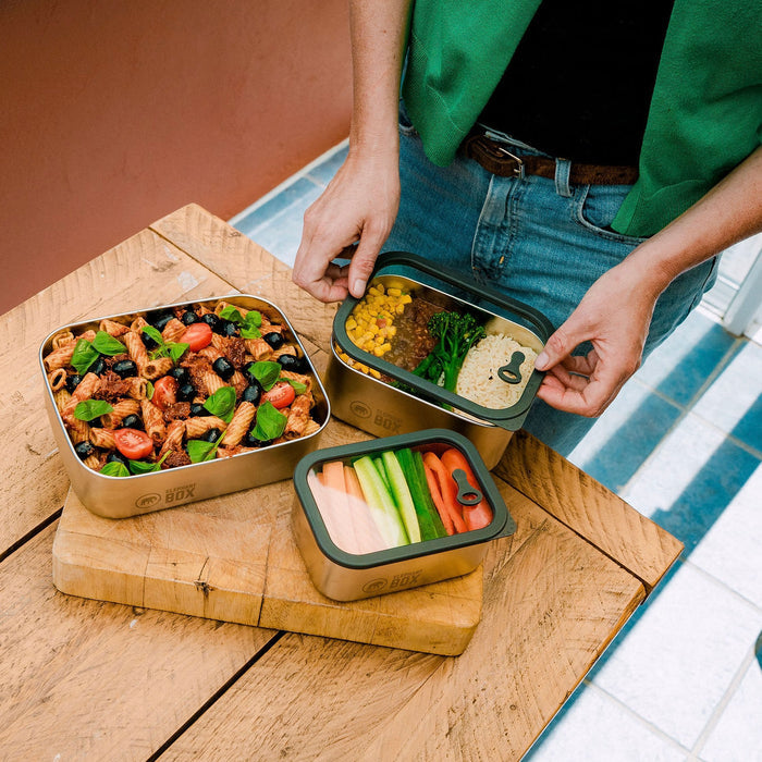Person opening a set of elephant Box prep and store food containers with various meals on a wooden board.