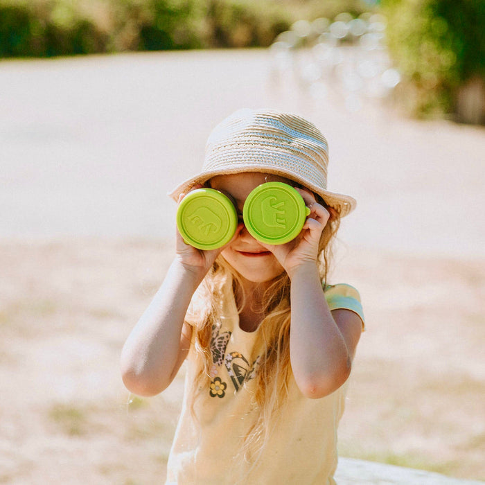 young girl holding up two stainless steel snack pots with elephant logo on lime green lid