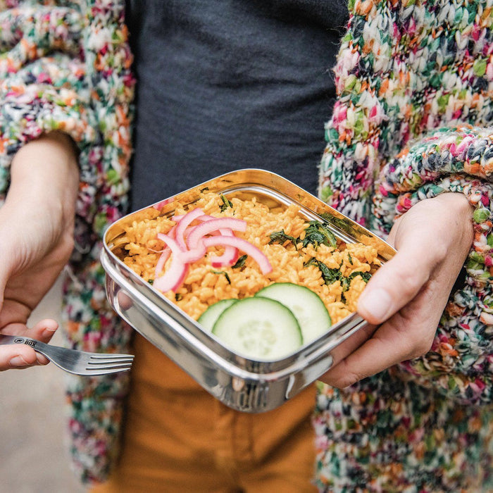 a person holding a square lunch box with their lunch inside